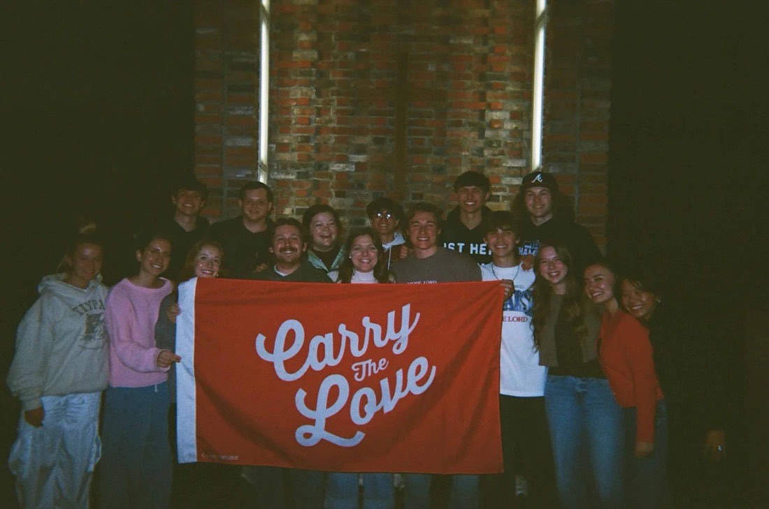 The outreach team holding a red Carry the Love flag at night in front of a brick church